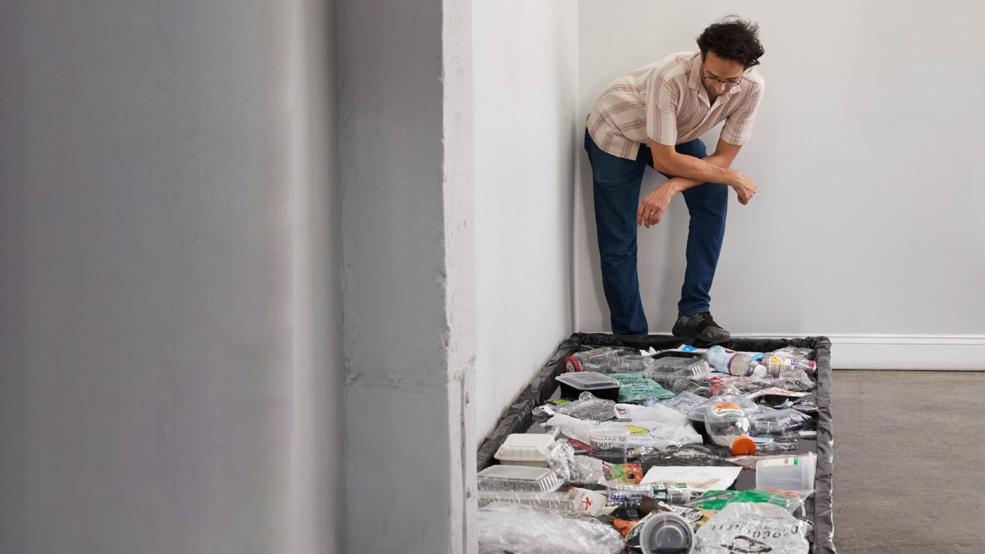 Photograph of a man (the artist) looking down on a black, rectilinear, floating pool of plastic trash
