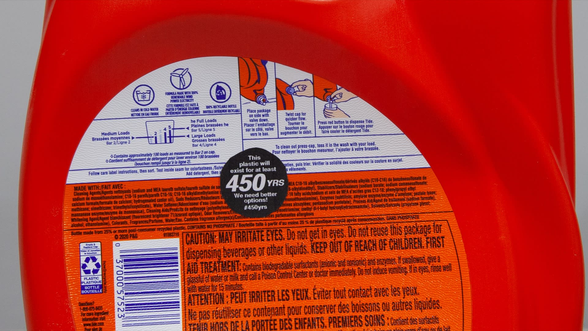 Thumbnail of Close-up of the previous photograph. Namely, a close up of a large, red, plastic laundry detergent bottle sitting on a workbench. In the middle of the bottle is a 1.5 inch, circular sticker that says, 'This plastic will exist for at least 450YRS. We need better options! #450yrs '