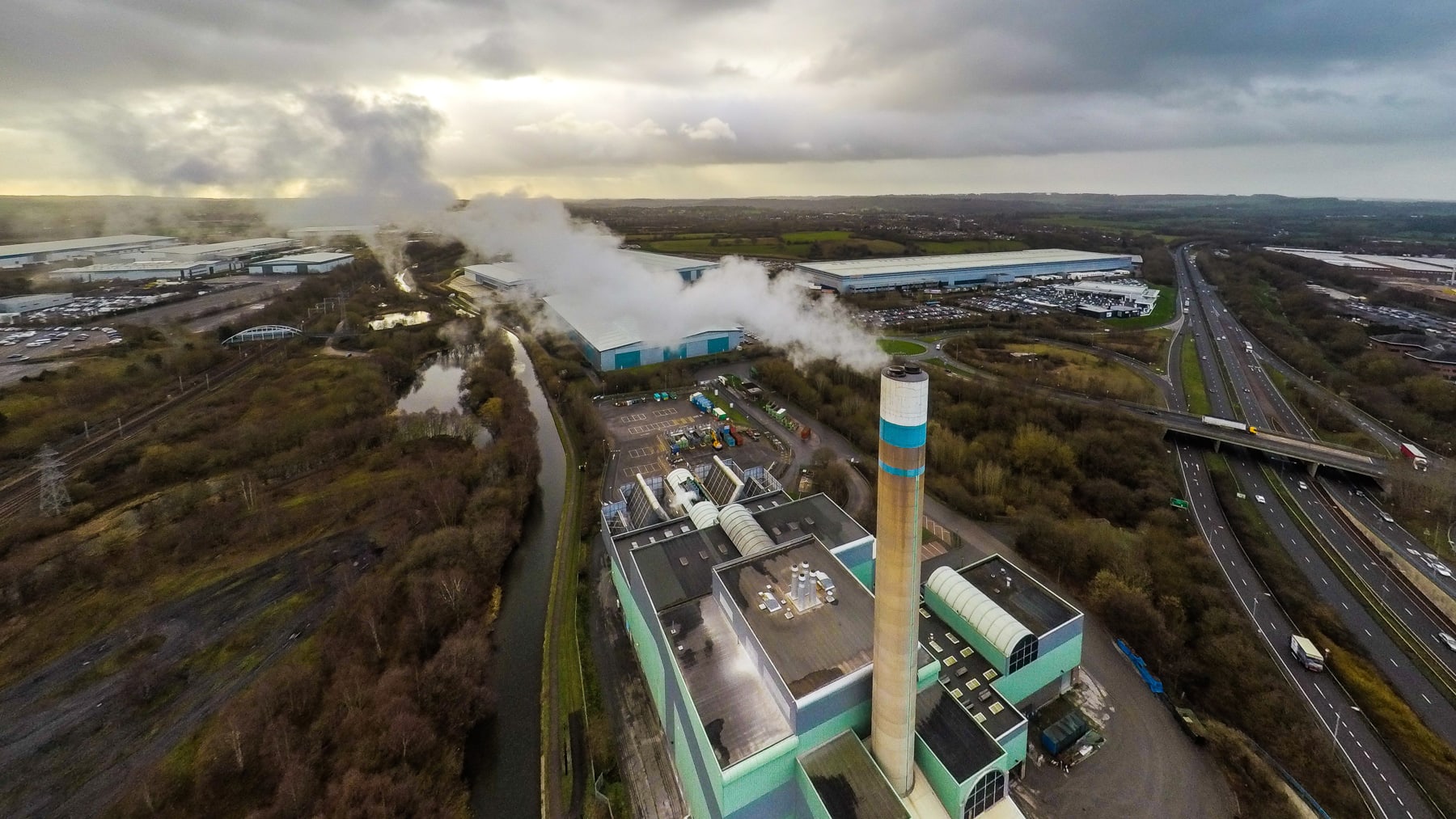 Aerial photograph of an incinerator, with one of its smoke stacks emitting a trail of smoke