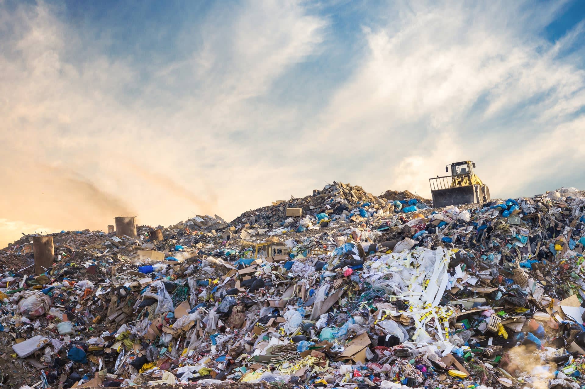 photo of a bulldozer on top of a giant pile of garbage in a landfill