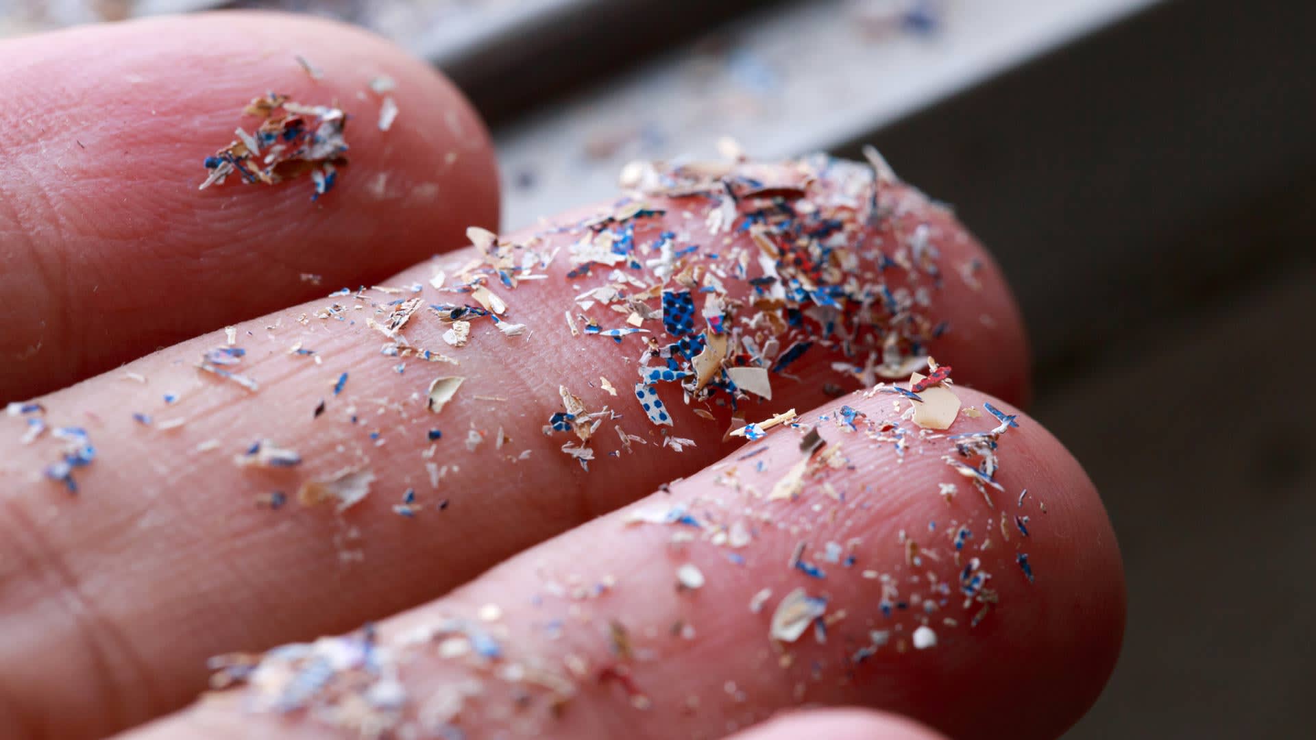 Close up of an hand with hundreds of specs of multi-colored microplastics