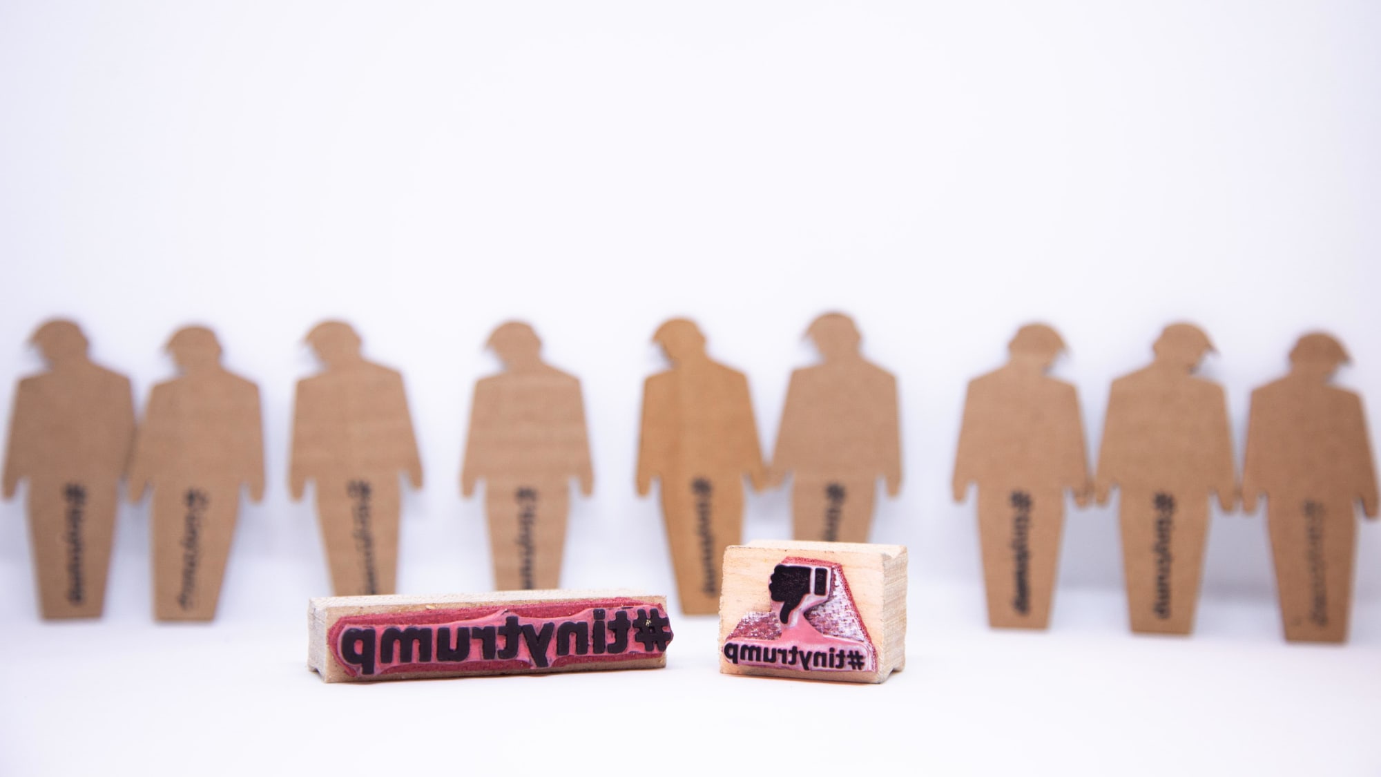 Photograph of 12 blank tiny trumps in the background and a rubber stamp with a thumbs down sign in the foreground