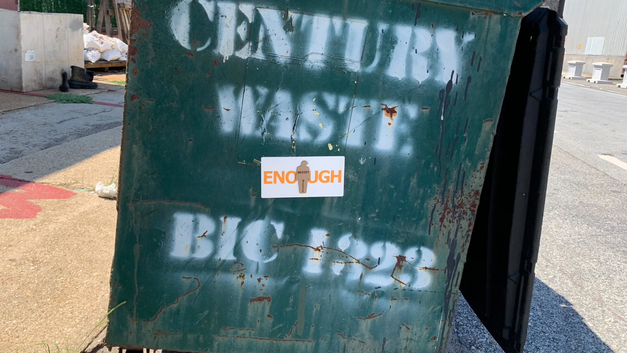Small thumbnail image of Photograph of a tiny trump ENOUGH sticker on a dumpster in the street. The tiny trump stuck in the middle bears the slogan Sexist, so the combination reads ENOUGH Sexist