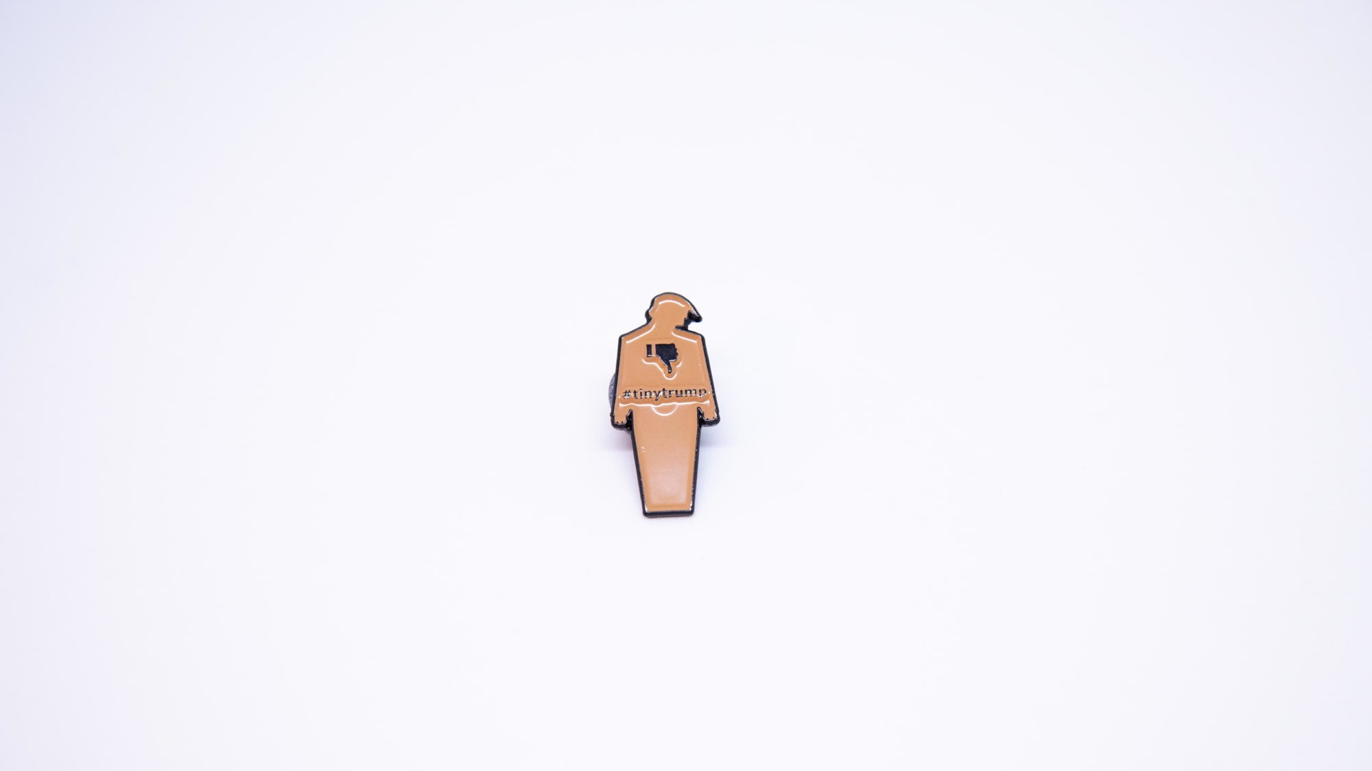 Photograph of a brown tiny trump enamel pin with a thumbs down sign on the left lapel of a man's suit blazer