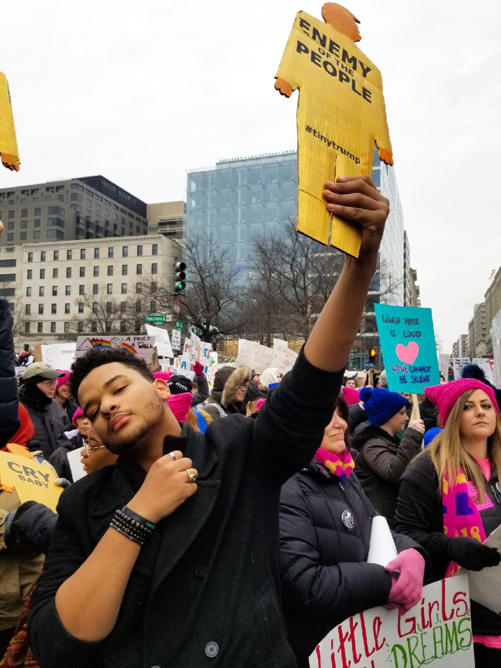 Photograph of a Black male holding a tiny trump high in the air in a sign of defiance