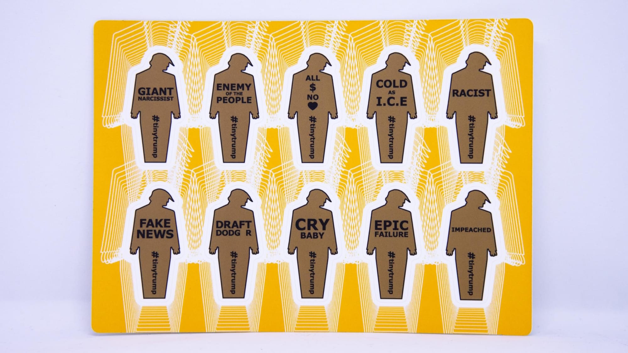 Small thumbnail image of Product photograph of a 4 inch by 6 inch sticker sheet consisting of a yellow background and 12 individual tiny trumps with the following slogans: Pussy Grabber, Putins Little Bitch, Doesnt Keep Us Safe, Fux News, Anti Science, Danger-US, Divider in Chief, I Dont Take Responsibility At All, Family Separator, Cheated on Wife, Taxes, Country