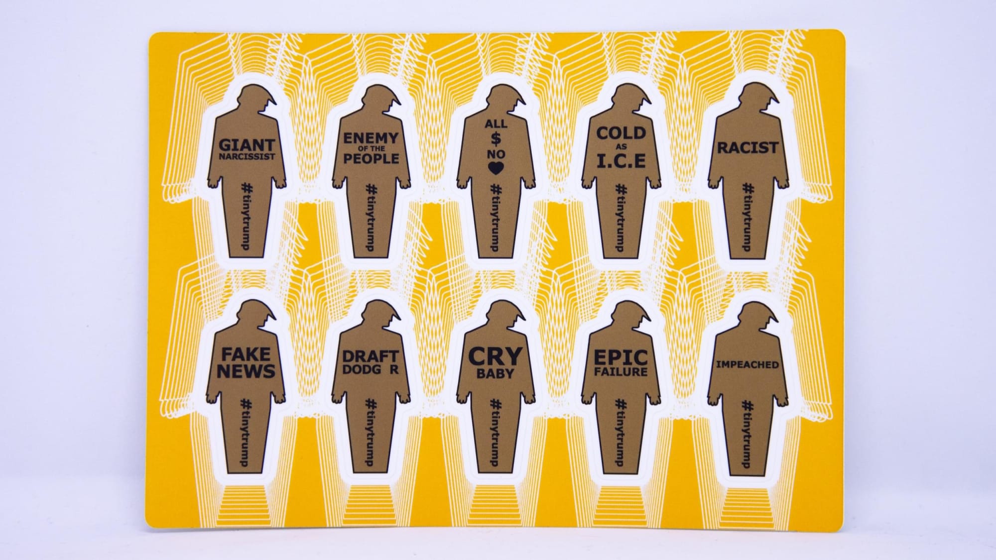 Product photograph of a 4 inch by 6 inch sticker sheet consisting of a yellow background and 12 individual tiny trumps with the following slogans: Pussy Grabber, Putins Little Bitch, Doesnt Keep Us Safe, Fux News, Anti Science, Danger-US, Divider in Chief, I Dont Take Responsibility At All, Family Separator, Cheated on Wife, Taxes, Country