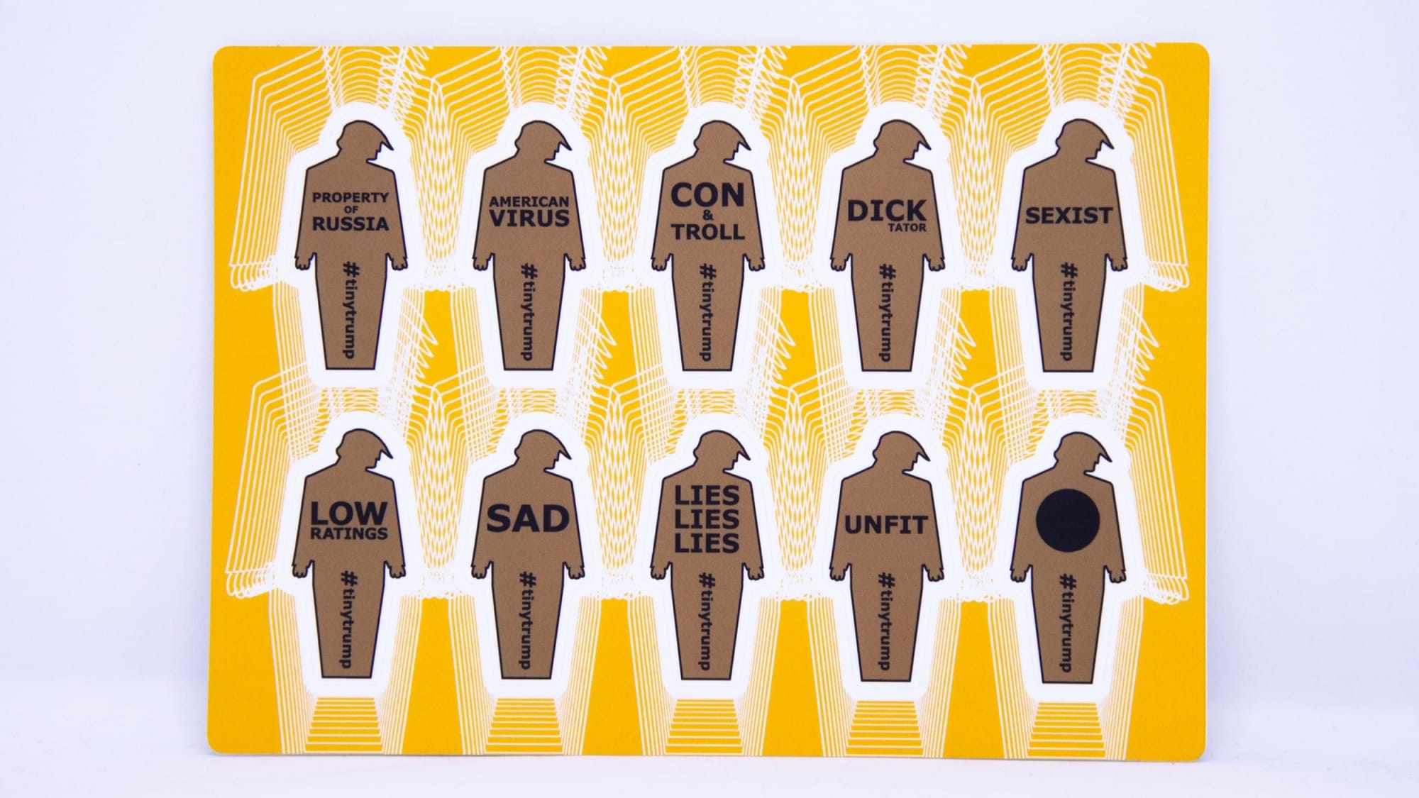 Small thumbnail image of Product photograph of a 4 inch by 6 inch sticker sheet consisting of a yellow background and 12 individual tiny trumps with the following slogans: Giant Narcissist, Enemy of the People, All money no heart, Cold as I.C.E, Racist, Fake News, Draft Dodger, Cry Baby, Epic Failure, Impeached