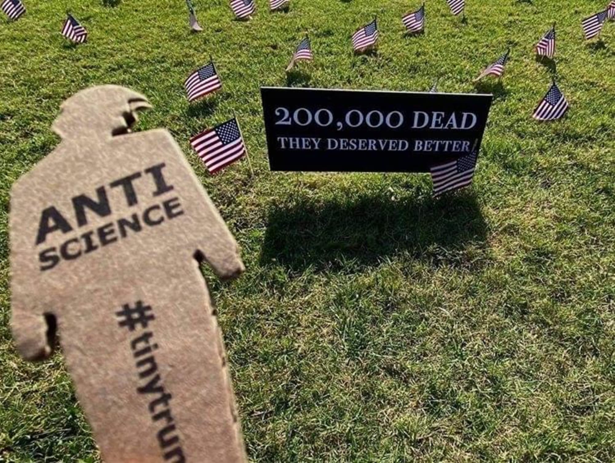 a photograph of a tiny trump with the slogan 'Anti-Science' held in front of a sign that reads '200,000' dead, they deserved better