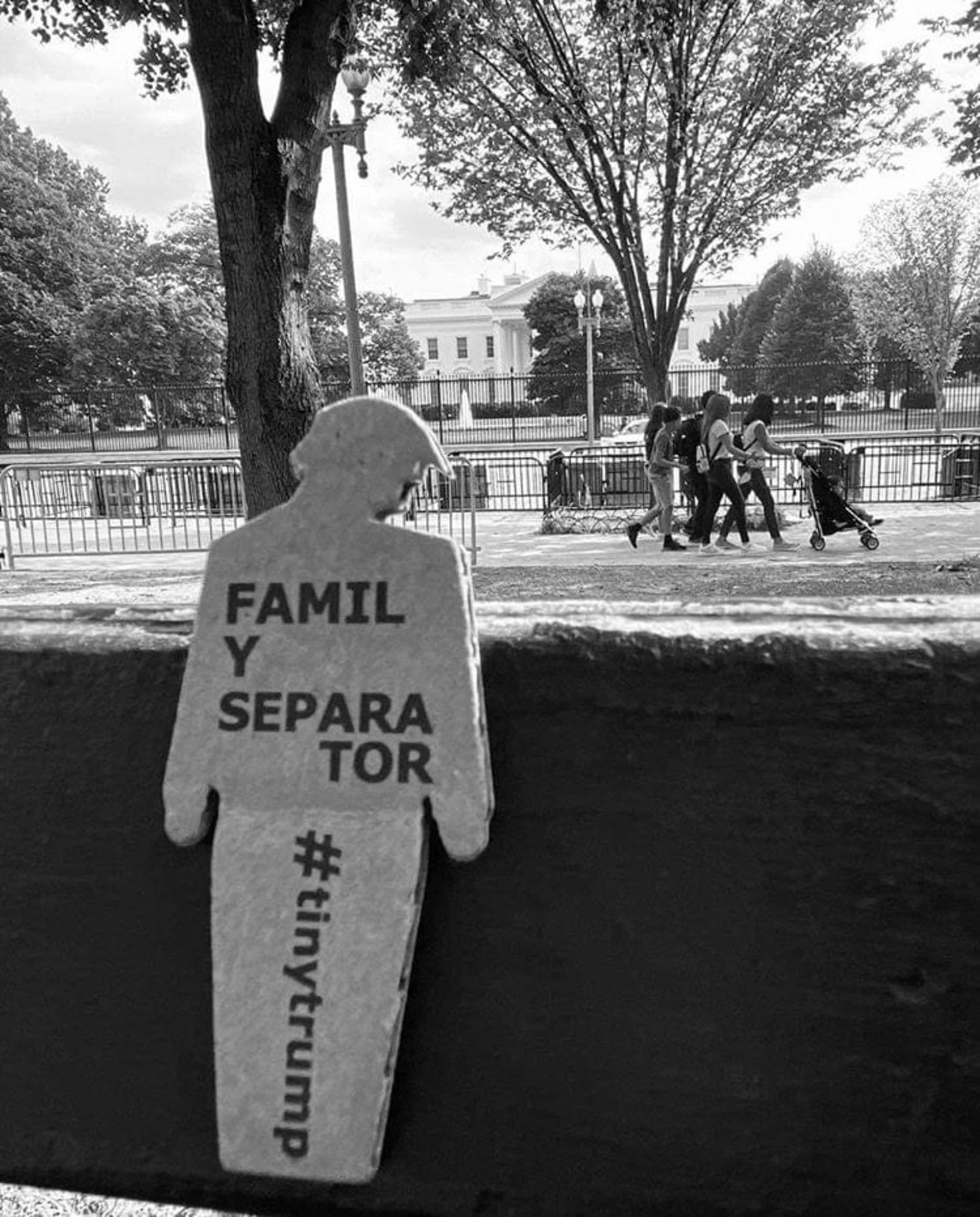 a black and white photo of a tiny trump with the slogan 'Family Separator' in the foreground; children playing in the background